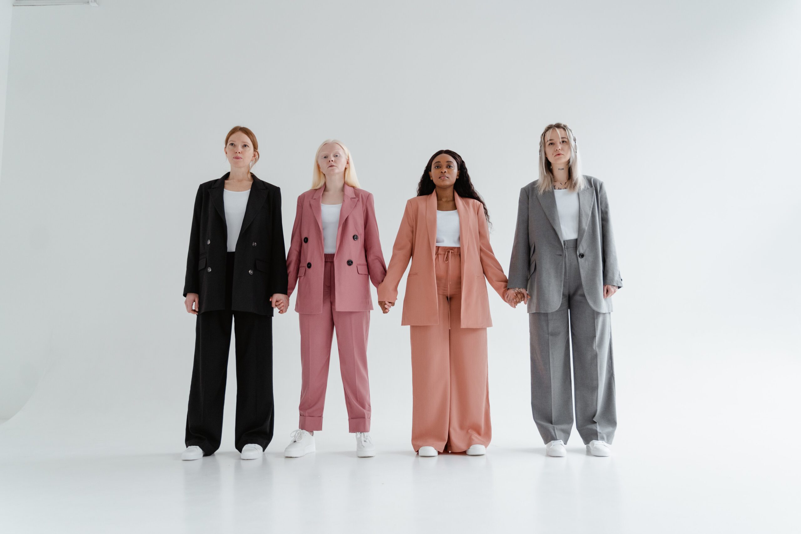 Cztery kobiety trzymające się za ręce w kolorowych garniturach z szerokimi spodniami