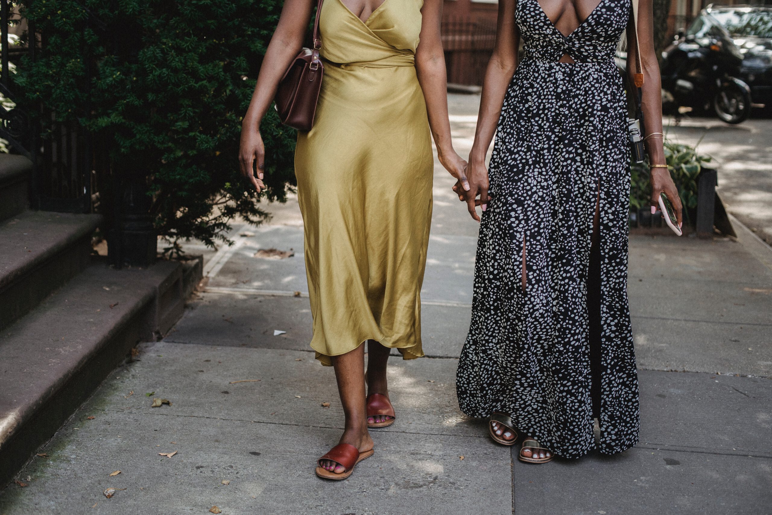 Dwie kobiety w różnych dlugch sukienkach trzymające się za ręce na spacerze