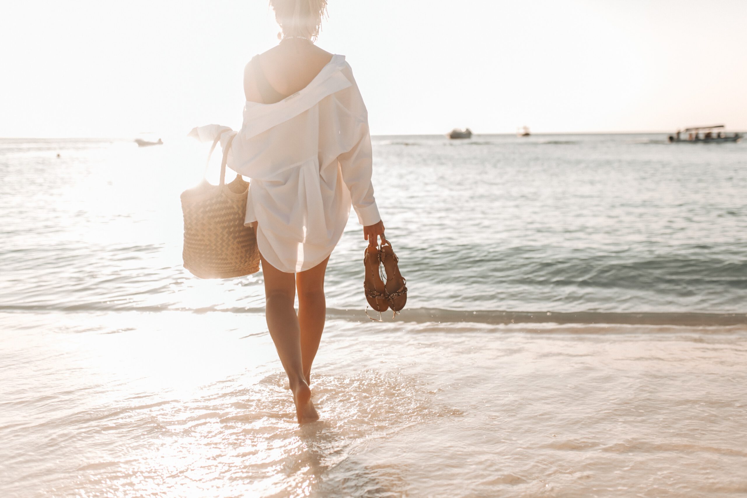 Kobieta na plaży w białej koszuli narzoconej na bieliznę stojąca tyłem